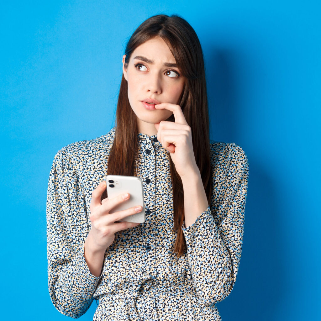 woman thinking while holding smartphone — representing why businesses choose RuhMark for digital marketing services